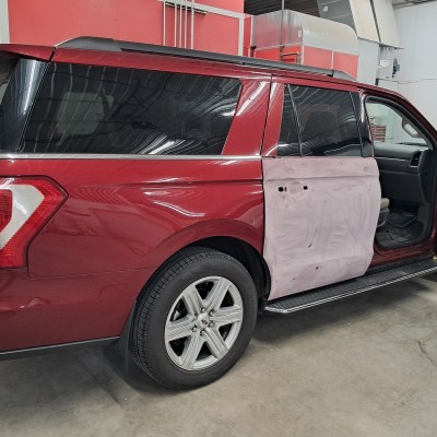 Repair and painting of the back passenger door on a red SUV