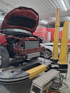Auto body repair work on red vehicle up on lift