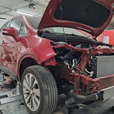 Major collision repair work on red vehicle up on a lift